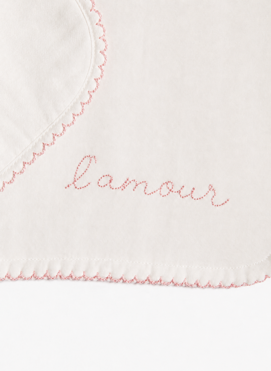 Close-up of a white fabric item with pink scalloped stitching and the word 'amour' embroidered in pink script across the center.