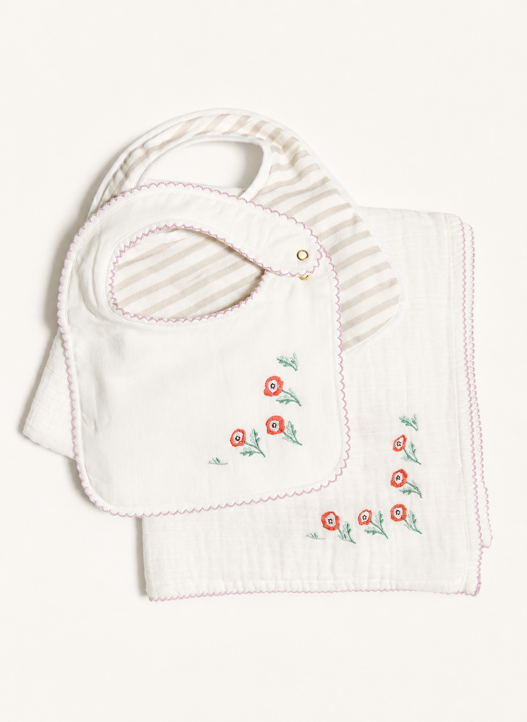 A baby gift set featuring a white cotton bib with pink trim and embroidered red flowers, layered over a matching white muslin cloth with a striped inner bib insert.