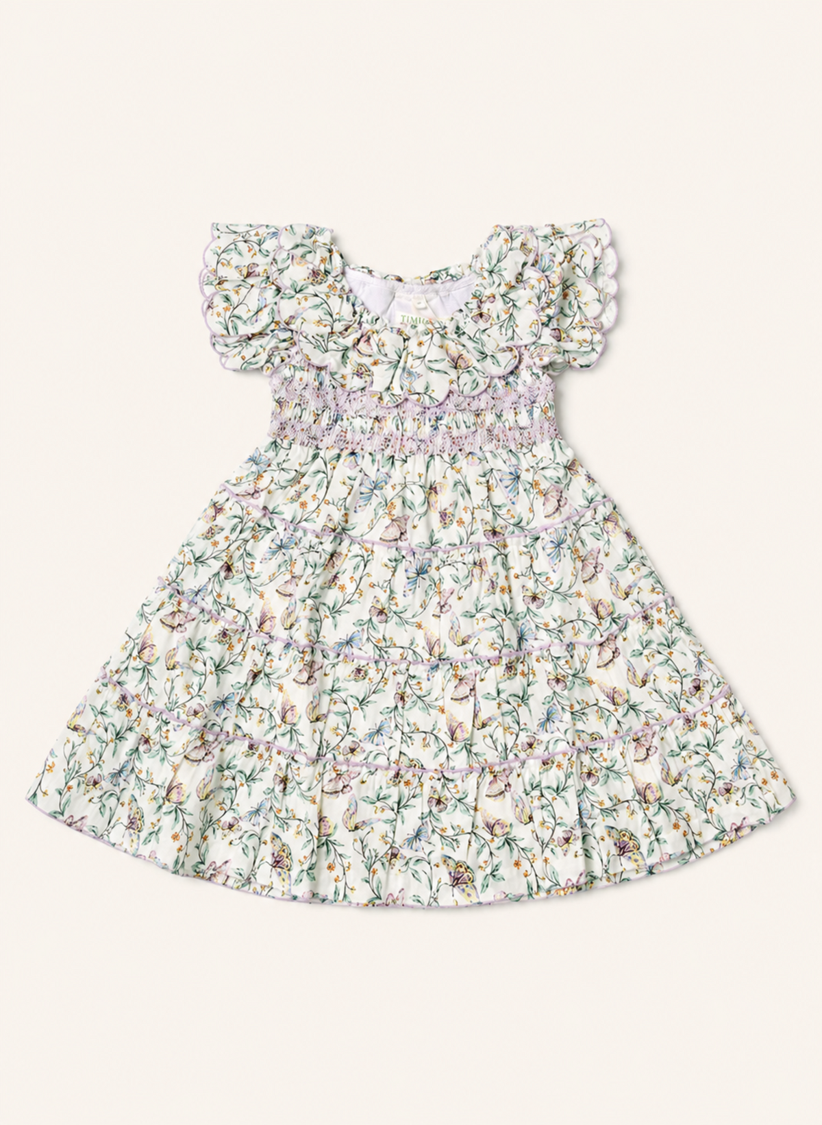 A toddler girl's ruffled dress with a delicate multicolor floral print on a cream background, featuring a smocked waist and flutter sleeves, shown flat on a light beige background.