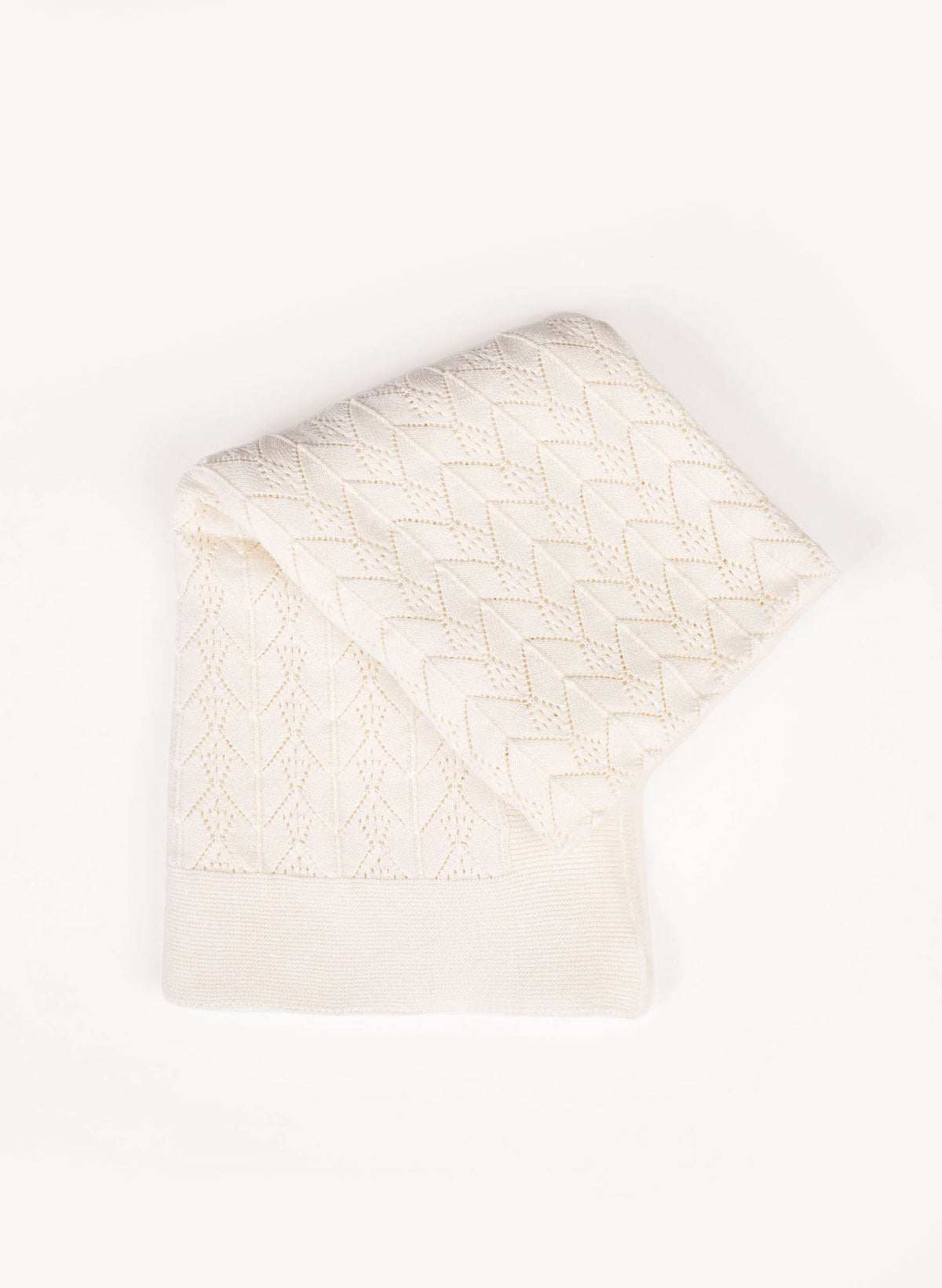 An off-white knit blanket with a textured chevron and diamond pattern, folded neatly on a clean white background.