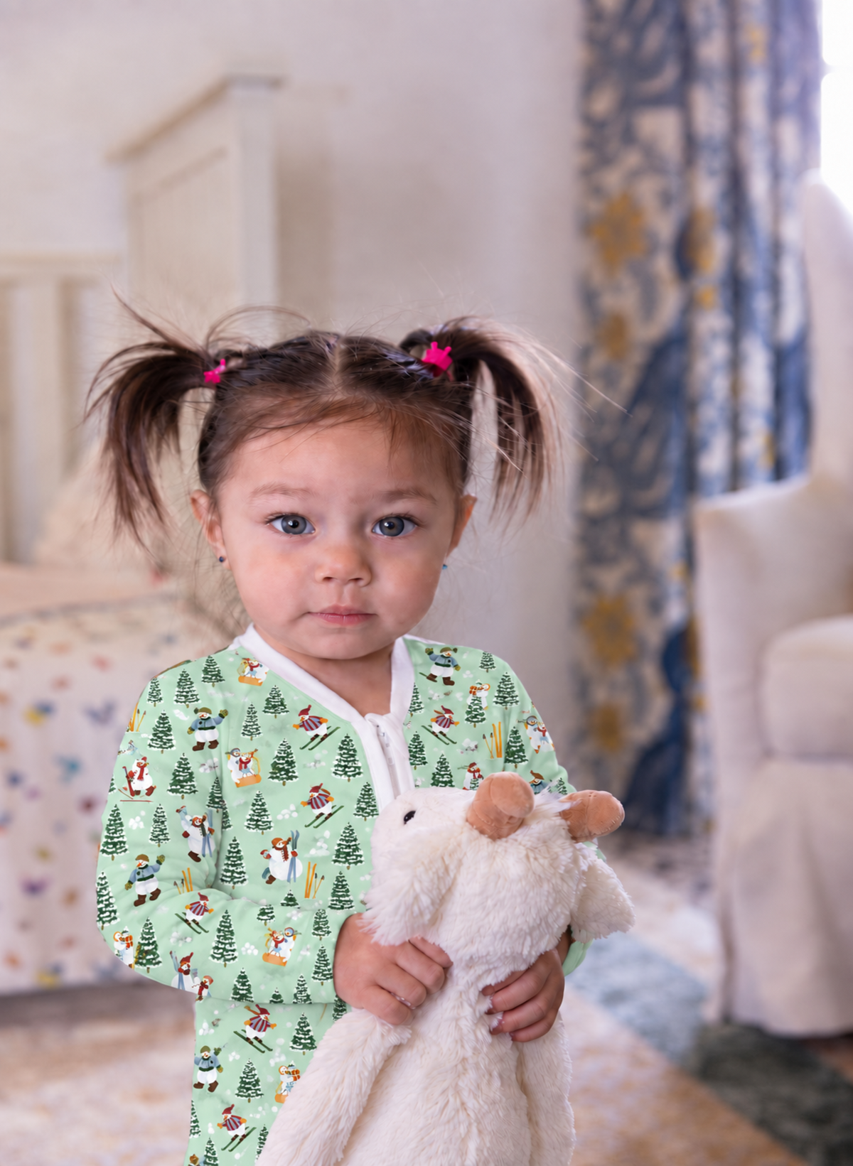 A young child with brown pigtails wearing a light green pajama shirt with a woodland animal print, holding a white plush toy in a softly lit bedroom.