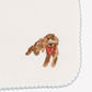 Close-up of a white baby bib with scalloped edges and an embroidered brown dog wearing a red polka-dot bandana.