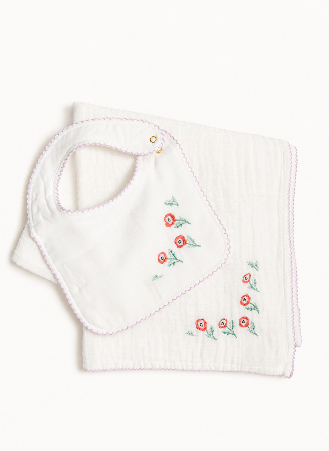 A white muslin baby bib with pink scalloped edges and embroidered red flowers with green leaves, shown folded on a white background.