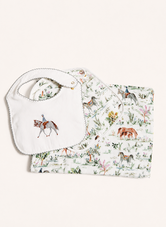 A baby gift set featuring a white fabric bib with a scalloped edge and embroidered horse design, paired with a matching printed muslin cloth showing a watercolor-style animal and nature pattern.