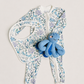 A baby zip-front footed one-piece outfit in an allover blue and purple underwater coral print, shown with a matching bib and a small blue octopus plush toy on a light beige background.