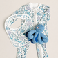 A baby outfit set featuring a white one-piece jumpsuit with a blue and purple sea-creature print, a matching bib, and a blue octopus plush toy, arranged on a light beige background.