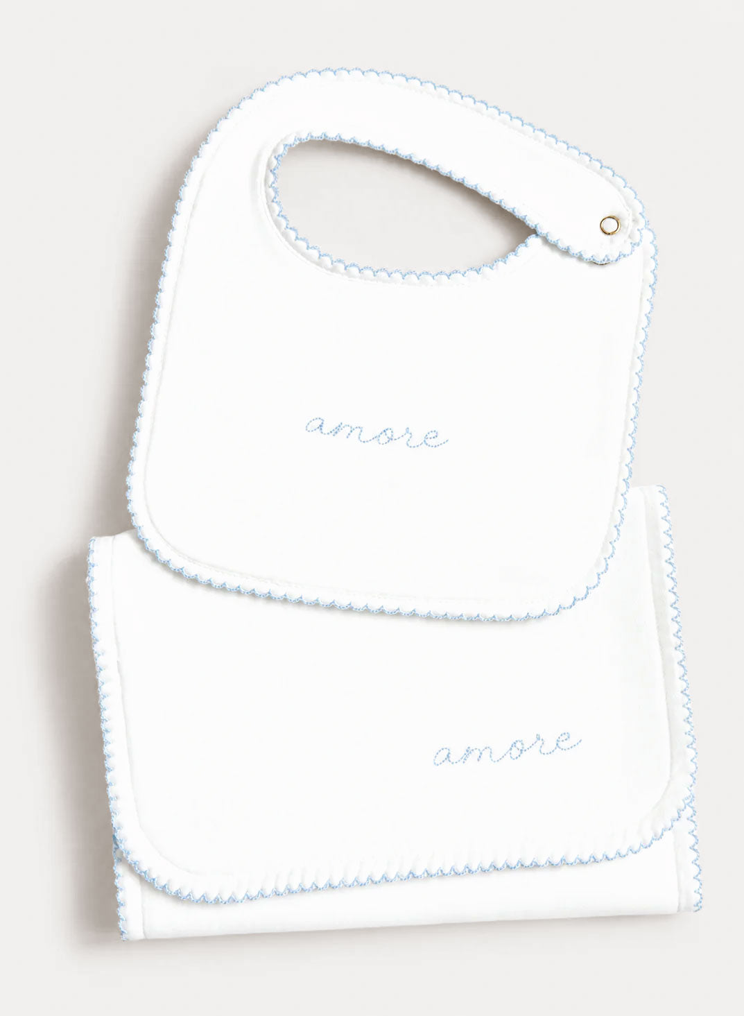 A white baby bib and matching folded cloth napkin set, both embroidered with the word 'amore' in light blue script and finished with a light blue scalloped edge.
