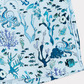 A close-up of a light blue fabric printed with an underwater ocean theme, featuring octopuses, fish, and coral in shades of blue, navy, and black.