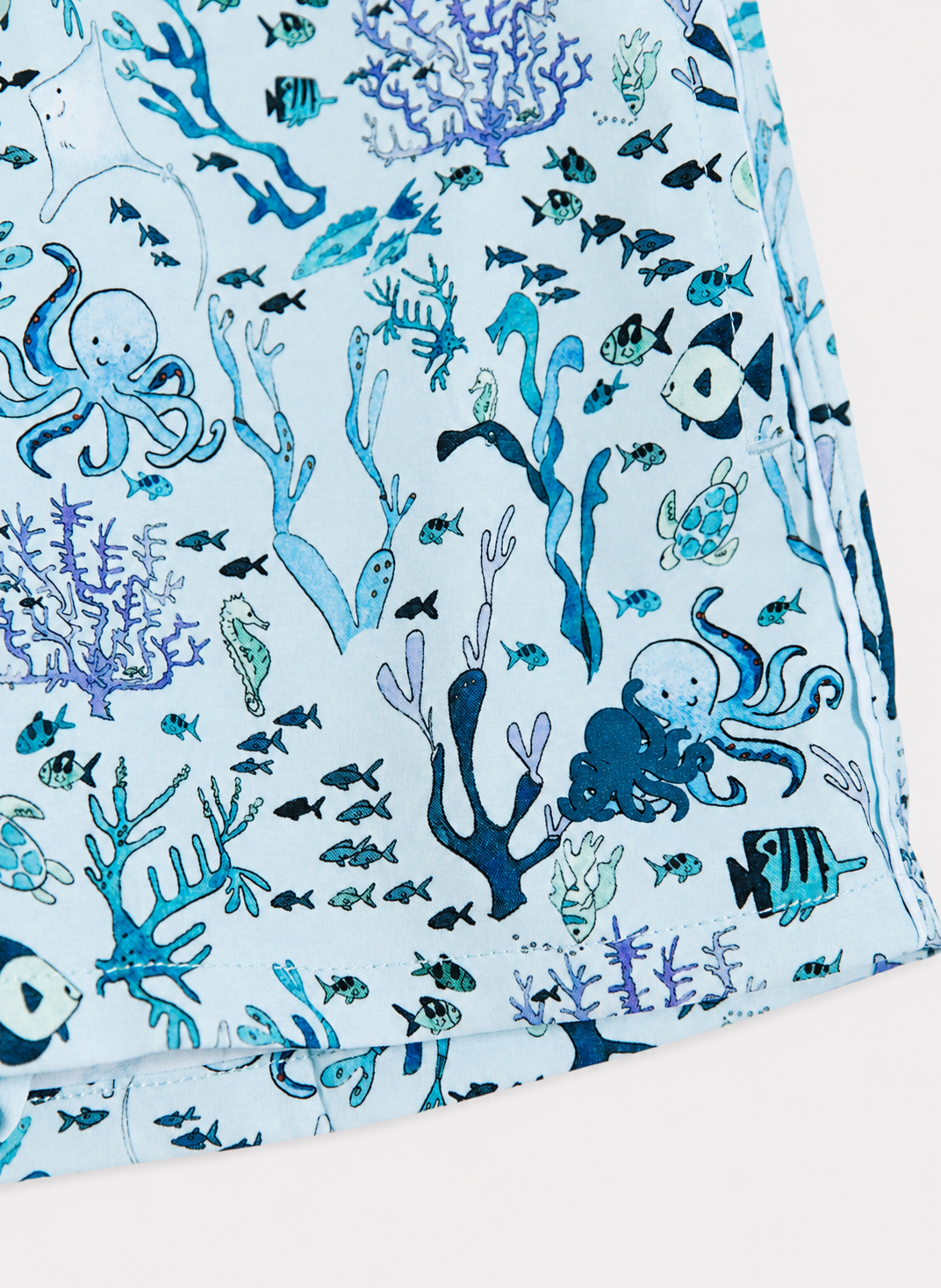 A close-up of a light blue fabric printed with an underwater ocean theme, featuring octopuses, fish, and coral in shades of blue, navy, and black.