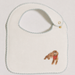An off-white baby bib with a scalloped edge, featuring a small embroidered brown dog wearing a red bandana in the bottom right corner.