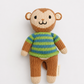 A handmade knitted monkey doll with a brown and beige body, wearing a green and blue striped sweater, photographed against a clean white background.
