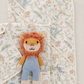 A soft baby blanket set with a white background and a delicate multicolor floral and animal print, styled with a small knitted lion plush toy.