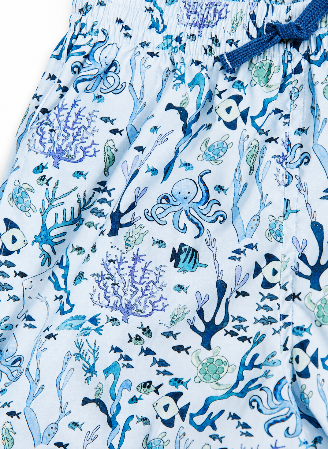 Close-up of a pair of shorts with an all-over underwater print featuring octopuses, fish, sea corals, and sea turtles in shades of blue, navy, and light green on a white background.