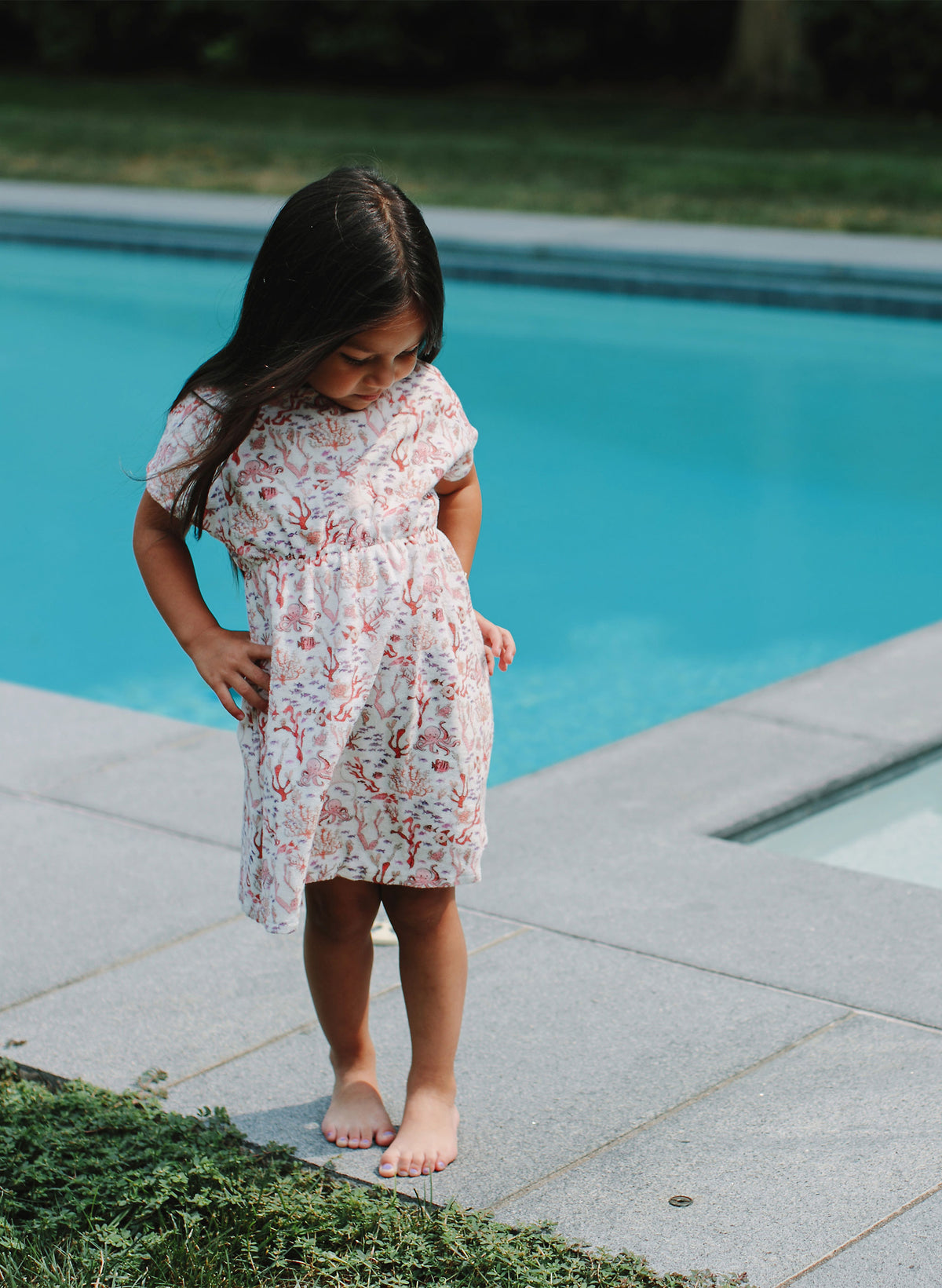 Young girl in a floral dress standing by a pool