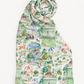 A lightweight scarf with a detailed, whimsical toile-style print featuring golf course scenes, dogs, people, umbrellas, and houses in soft green, beige, and blue tones, rolled at the top against a plain white background.