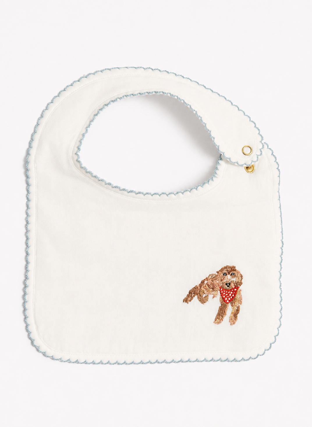 An off-white baby bib with a scalloped light blue border, featuring a small embroidered brown dog wearing a red bandana on the lower right.