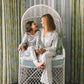 Two women sitting on a wicker chair in a room with patterned curtains.