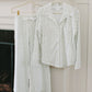 White textured shirt and pants hanging on a hanger against a white wall.