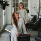 A woman and a young girl wearing matching floral pajama sets pose together in a bright, modern room with stone tile floors and large white French doors.