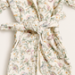 A close-up of a quilted bathrobe with a tie belt, featuring a delicate floral and butterfly pattern in soft pastel colors on an off-white background.