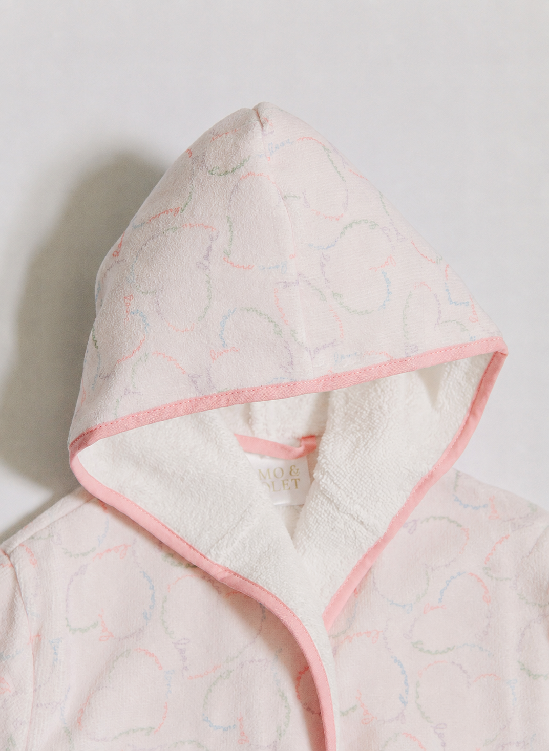 A close-up of a girl's hooded robe or towel set in a very light pink fabric with a subtle tonal cloud pattern, featuring a contrasting soft pink inner lining and trim.