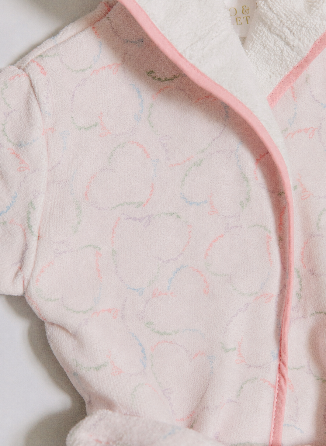 A close-up of a plush white bathrobe with a soft pink border and a subtle, tonal heart pattern.