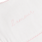 Close-up of a white fabric item with pink scalloped trim and the word 'amour' embroidered in pink script across the center.