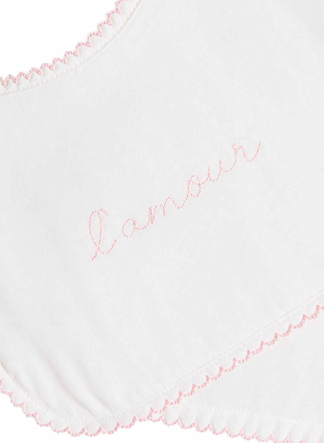Close-up of a white fabric item with pink scalloped trim and the word 'amour' embroidered in pink script across the center.