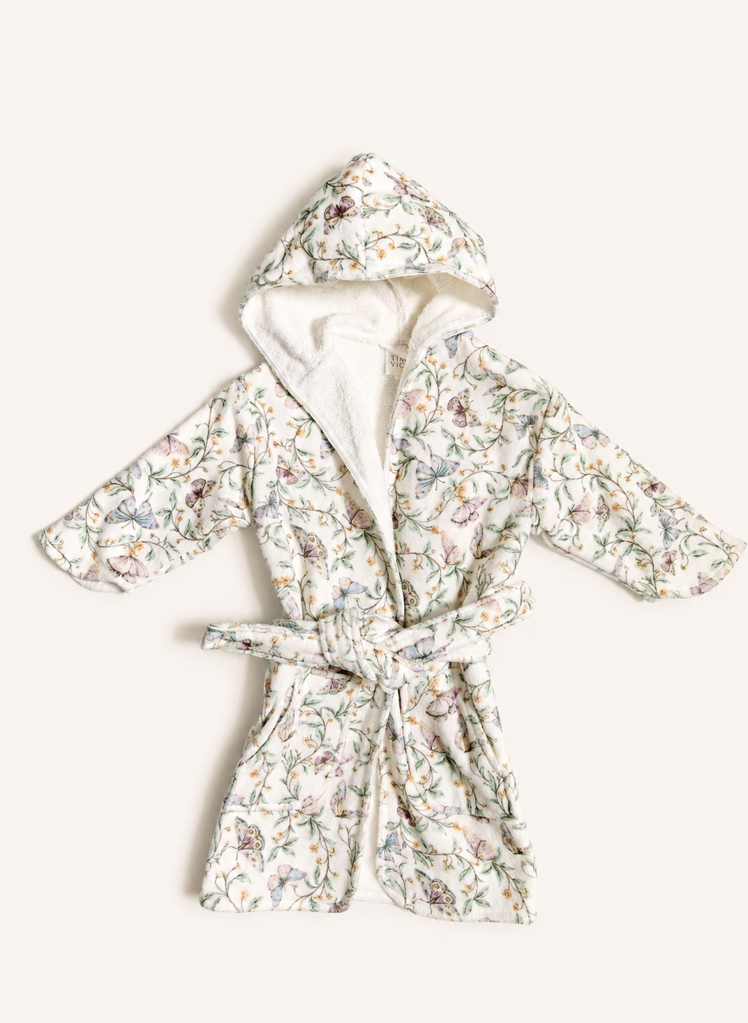 A hooded bathrobe with a white sherpa lining and a delicate multicolor floral print, tied at the waist, laid flat on a light cream background.