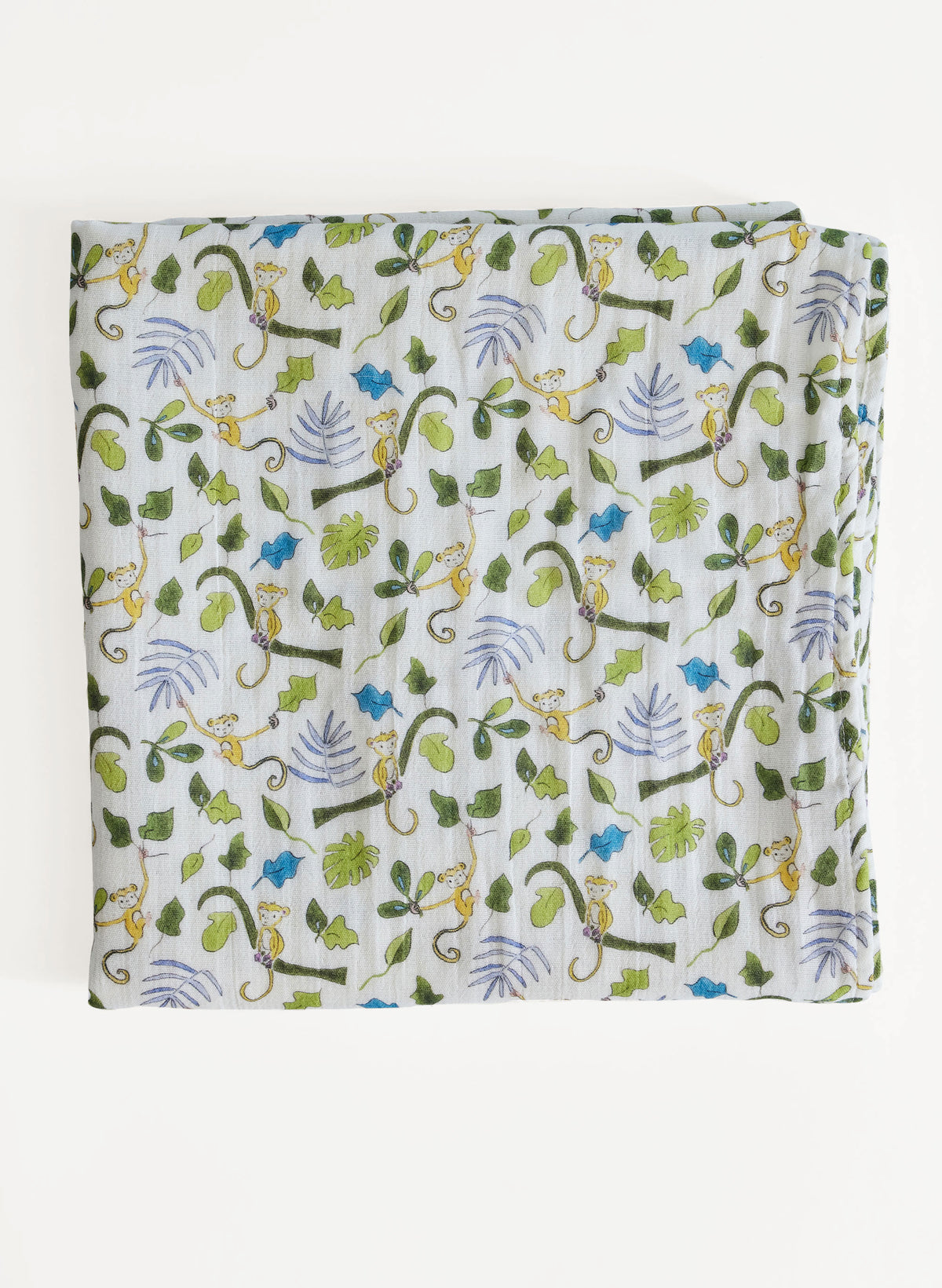 A folded white muslin blanket featuring a colorful repeating pattern of green leaves, blue flowers, and yellow monkeys, displayed against a clean white background.
