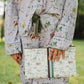 A person wearing a matching pajama set with an all-over horse and floral print, holding a matching clutch bag outdoors on a grassy lawn.