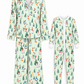 A matching pajama set shown on a white background, including a long-sleeve button-front top and pants set on the left, and a one-piece pajama set on the right. Both sets have a light mint green base with a festive Christmas print featuring pine trees, snowmen, Santa Claus, and snowmobiles.