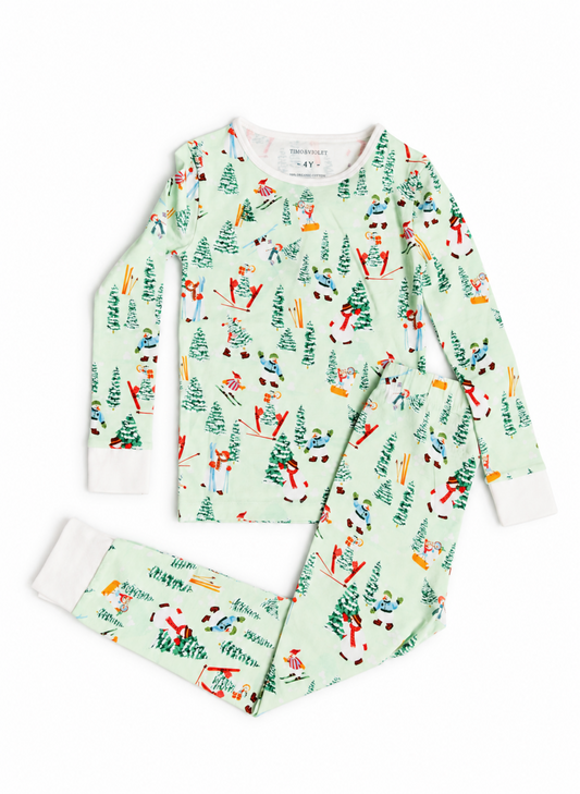 A two-piece children's pajama set from the brand Pajera, featuring a long-sleeve top and matching pants in a light mint green color with a colorful winter ski and Christmas tree pattern. The cuffs and collar are solid white.