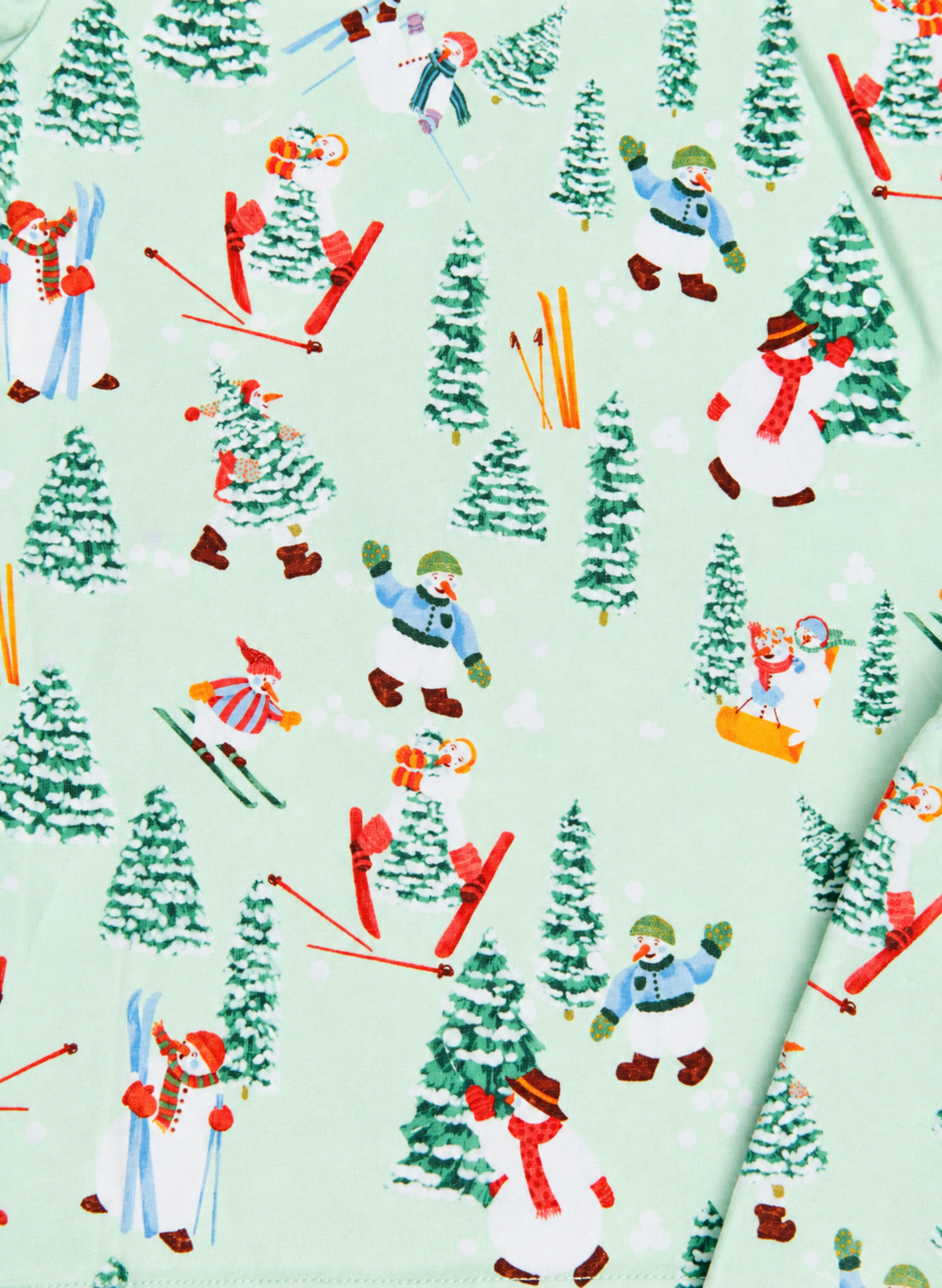 A close-up of a light mint green fabric printed with a winter ski and snowboard pattern featuring cartoon characters, pine trees, and skis.