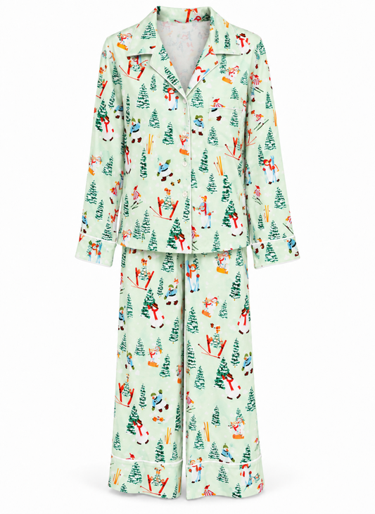 A two-piece pajama set featuring a long-sleeve button-front top and matching wide-leg pants, both in a pale mint green fabric with a colorful winter-themed print of skiers, snowboarders, and Christmas trees.