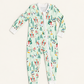 A baby's long-sleeve zip-up footed sleeper with a festive winter print of skiers, snowboarders, and Christmas trees on a pale mint green background, shown flat on a light cream background.