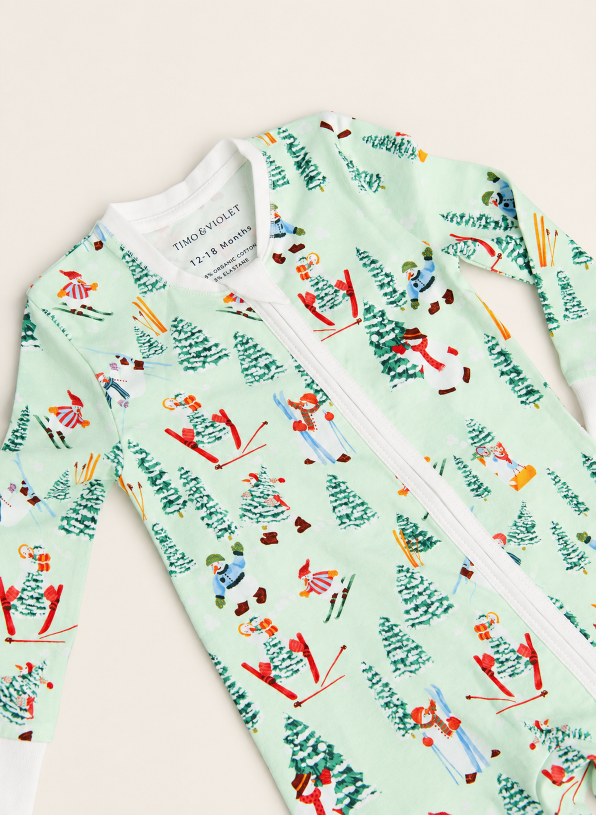 A long-sleeve baby zip-up sleeper by Tim & Mary in mint green, featuring a colorful allover print of skiers, snowboarders, and skis.