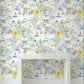A room interior showing a wall covered in a pastel toile-style wallpaper pattern with houses, boats, flowers, and plaid motifs. A white console table is placed in front of the wall, with dark wood flooring visible at the bottom.