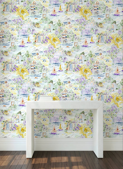 A room interior showing a wall covered in a pastel toile-style wallpaper pattern with houses, boats, flowers, and plaid motifs. A white console table is placed in front of the wall, with dark wood flooring visible at the bottom.
