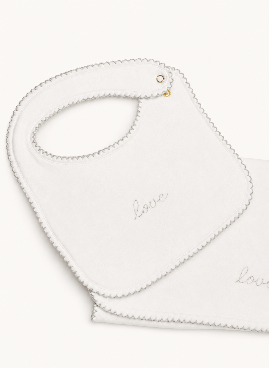 A white baby bib with a scalloped edge and the word 'love' embroidered in gray script, shown on a clean white background.