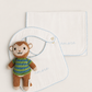 Two white muslin baby bibs with light blue scalloped edges and embroidered 'amore' script, styled with a small knitted monkey doll on a warm off-white background.