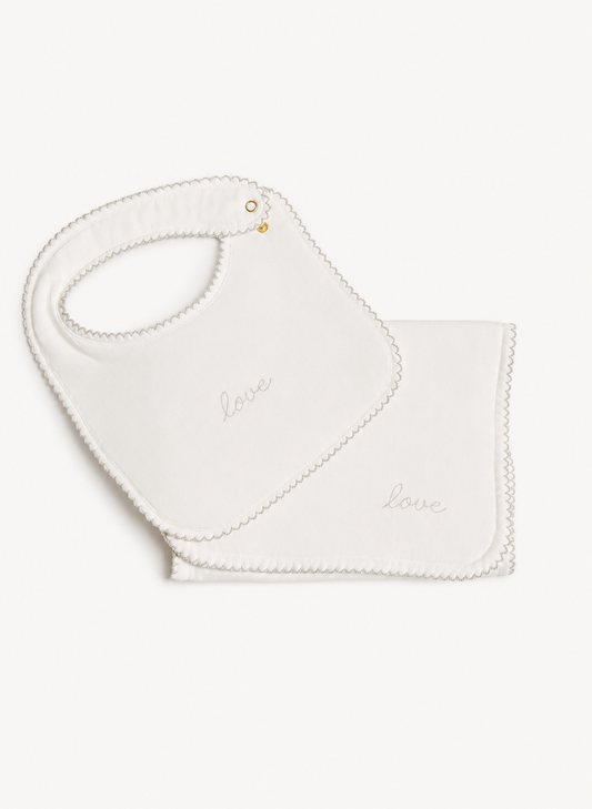A white baby bib and matching square cloth with scalloped edges and the word 'love' embroidered in script, shown on a plain light background.