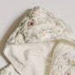 A close-up of a hooded garment, likely a robe or blanket, featuring a cream-colored outer fabric with a delicate pastel floral and butterfly print, and a plush cream sherpa lining.