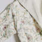 Close-up of a soft fleece or plush robe with a white border and a delicate pastel butterfly and floral print on an off-white background.