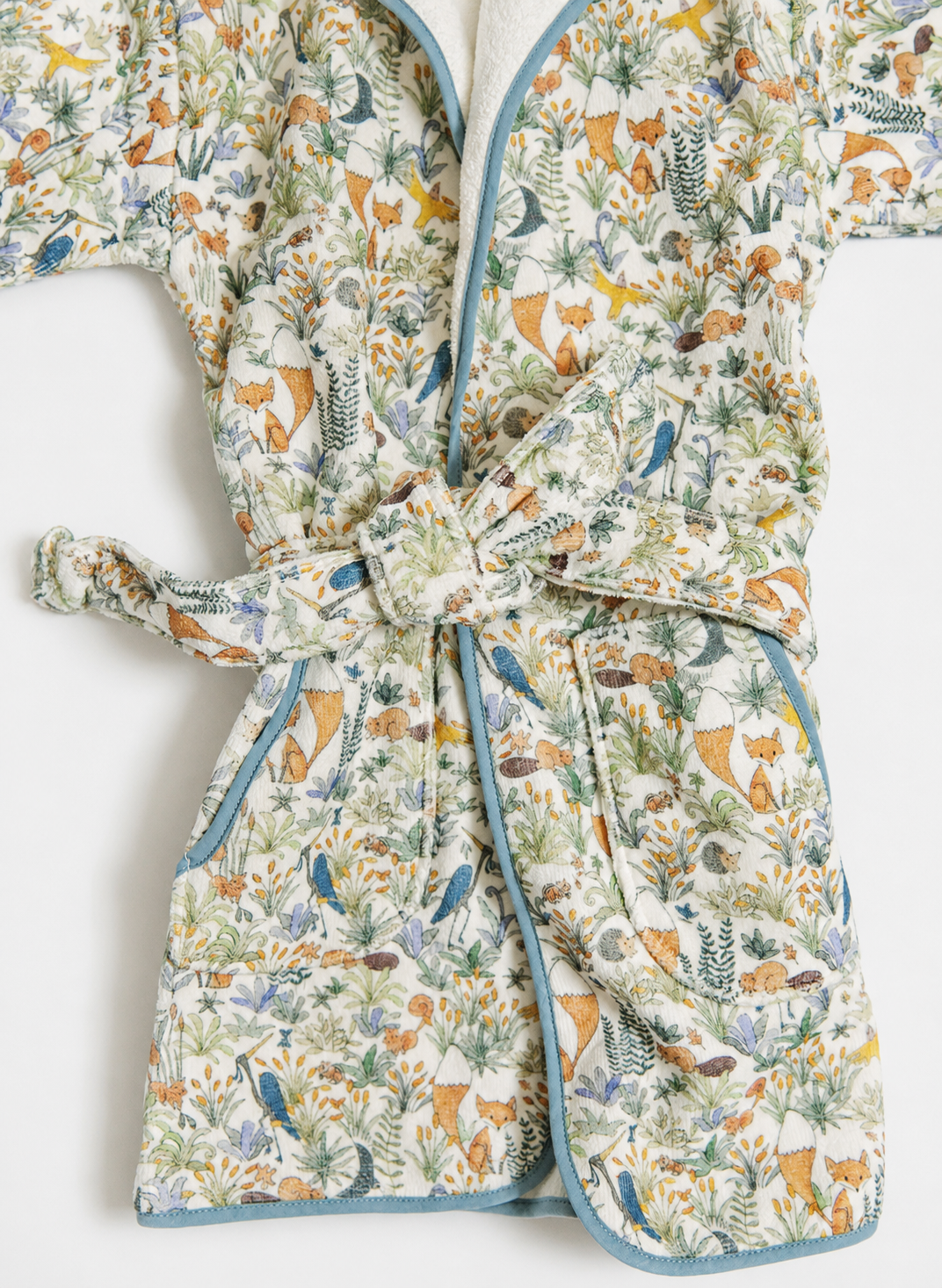 A quilted cotton robe with a woodland animal and plant print, featuring blue-green piping and a matching tie belt.