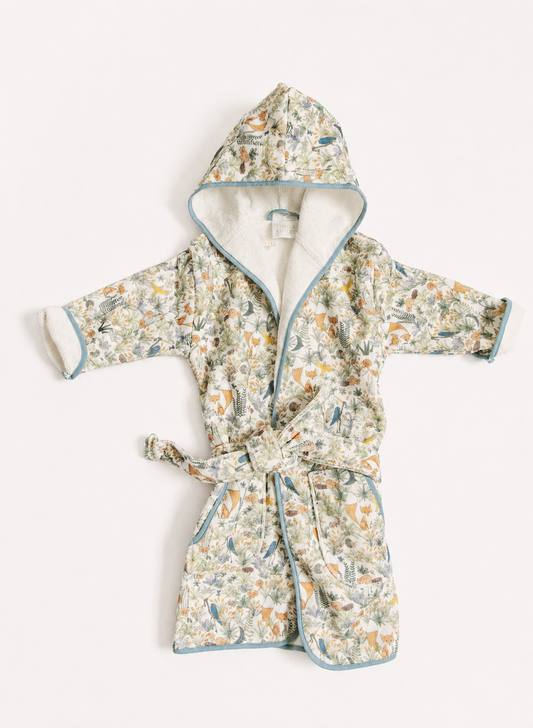 A children's hooded bathrobe with a tie belt, featuring a delicate multicolor floral and botanical print on a light cream base, with light blue piping and a soft cream lining.