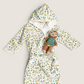 A baby hooded bathrobe with a colorful monkey and leaf pattern on a cream background, styled with a small plush monkey toy, laid flat on a light beige background.