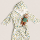 A baby hooded bathrobe with a colorful dinosaur print, styled with a small plush monkey toy, laid flat on a light beige background.