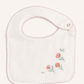 A white baby bib with a scalloped pink border and embroidered pink flowers with green stems on the lower right, shown on a light cream background.