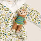 A baby hooded robe with a jungle-themed print in green, yellow, and blue on an off-white background, styled with a small plush monkey toy wearing a striped sweater.